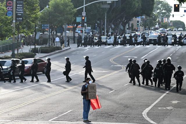 A protestor holds a sign reading "think, while it's still legal," as police move into position to clear the streets on June 14, 2025 in Los Angeles, California after the "No Kings" demonstration. Tens of thousands of protesters rallied nationwide Saturday against Donald Trump ahead of a huge military parade on the US president's 79th birthday -- as the killing of a Democratic lawmaker underscored the deep divisions in American politics. "No Kings" demonstrators took to the streets in New York, Los Angeles, Chicago, Philadelphia, Houston, Atlanta and hundreds of other cities across the United States to condemn what they call Trump's dictatorial overreach. (Photo by Robyn Beck / AFP)