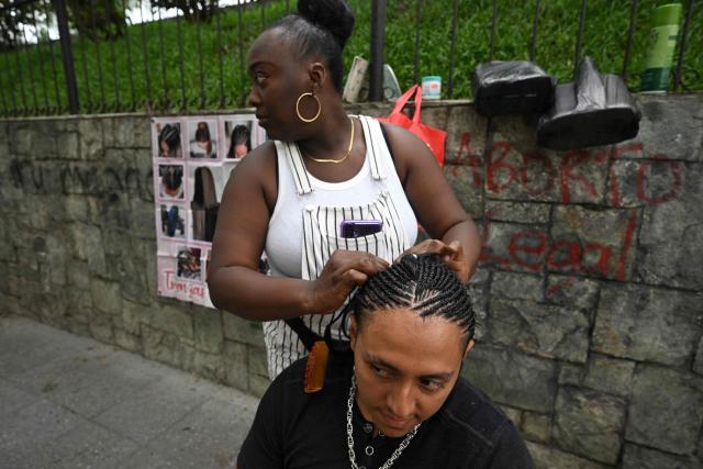 A woman braids a man's hair in the Historic Center in Guatemala City on June 15, 2025. (Photo by JOHAN ORDONEZ / AFP)