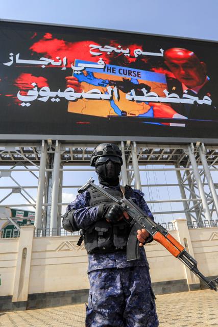 A member of security forces loyal to Yemen's Huthis stands guard while behind a giant screen shows a message lambasting Israel's Prime Minister Benjamin Netanytahu, during a rally organised by the Huthis' supporters in solidarity with Iran and Palestinians in the Gaza Strip while condemning Israel, in the Huthi-held capital Sanaa on June 20, 2025. (Photo by Mohammed HUWAIS / AFP)