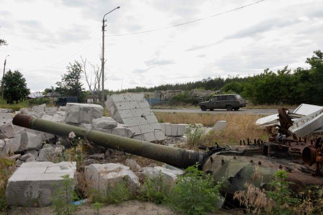 A car drives along the road past a partialy burnt tank in the city of Svyatohirs'k, Donetsk region on June 26, 2025, amid the Russian invasion of Ukraine. (Photo by Tetiana DZHAFAROVA / AFP)