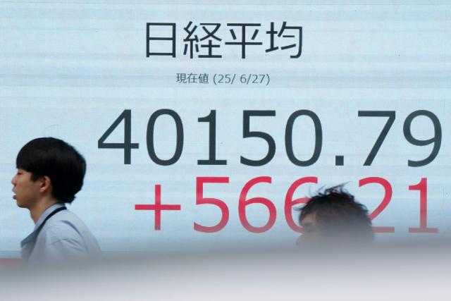 Pedestrians walk in front of an electronic quotation board displaying the Nikkei Stock Average closing price at 40,000 yen level on the Tokyo Stock Exchange in Tokyo on June 27, 2025. (Photo by Kazuhiro NOGI / AFP)