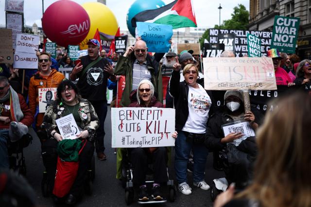 (FILES) Protesters sitting in wheelchairs hold placards reading messages like "Benefit cuts kill" as they take part in a "No More Austerity 2.0" march in central London on June 7, 2025, hosted by The People's Assembly Against Austerity. The UK government backed down on Friday, June 27, on controversial plans to slash disability and sickness benefits after a a major rebellion by MPs -- a blow to Prime Minister Keir Starmer's authority. (Photo by HENRY NICHOLLS / AFP)