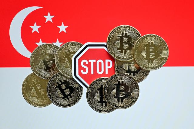 This illustration photograph taken on June 30, 2025 shows a stop sign amidst Bitcoin cryptocurrency representation coins against the backdrop of the Singapore national flag, in Bangkok. Singapore ramped up crypto exchange regulations on June 30, 2025 in a bid to curb money laundering and boost market confidence after a series of high-profile scandals rattled the sector. (Photo by MANAN VATSYAYANA / AFP)