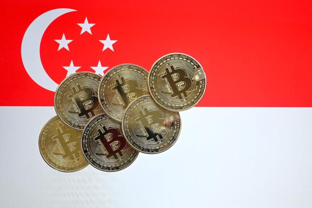 This illustration photograph taken on June 30, 2025 shows Bitcoin cryptocurrency representation coins against the backdrop of the Singapore national flag, in Bangkok. Singapore ramped up crypto exchange regulations on June 30, 2025 in a bid to curb money laundering and boost market confidence after a series of high-profile scandals rattled the sector. (Photo by MANAN VATSYAYANA / AFP)