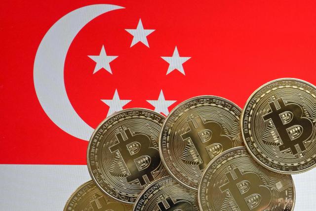 This illustration photograph taken on June 30, 2025 shows Bitcoin cryptocurrency representation coins against the backdrop of the Singapore national flag, in Bangkok. Singapore ramped up crypto exchange regulations on June 30, 2025 in a bid to curb money laundering and boost market confidence after a series of high-profile scandals rattled the sector. (Photo by MANAN VATSYAYANA / AFP)