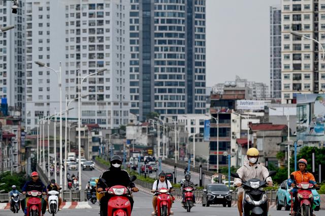 Motorbikes drive in front of high-rise buildings in Hanoi on June 30, 2025. (Photo by Nhac NGUYEN / AFP)