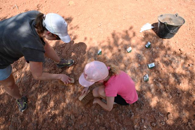 An adult and a child search for dinosaur eggs at the Mount Sainte-Victoire site, near Aix-en-Provence in southern France, on June 25, 2025. Armed with a hand brush, a paleontologist meticulously inspects a mound of red clay at the foot of Mount Sainte-Victoire, in search of very specific fossils dating back some 75 million years: dinosaur eggs. (Photo by Christophe SIMON / AFP)