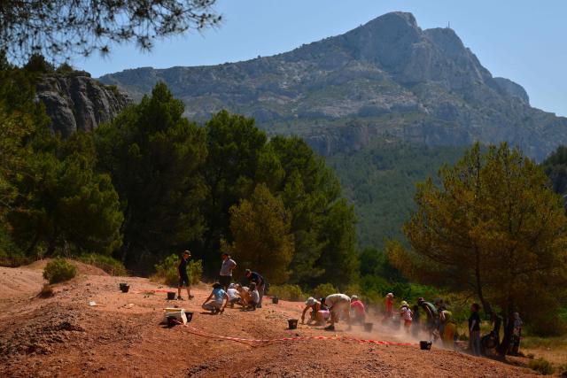 Adults and children search for dinosaur eggs at the Mount Sainte-Victoire site, near Aix-en-Provence in southern France, on June 25, 2025. Armed with a hand brush, a paleontologist meticulously inspects a mound of red clay at the foot of Mount Sainte-Victoire, in search of very specific fossils dating back some 75 million years: dinosaur eggs. (Photo by Christophe SIMON / AFP)