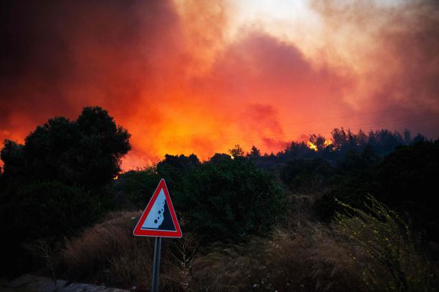 Smoke and flames rise from a forested area following a wildfire in the Seferihisar district of Izmir, Turkey, on June 30, 2025. Rescuers have evacuated more than 50,000 people, mostly from Turkey's western Izmir province, as firefighters battled a string of wildfires, the AFAD disaster agency said Monday. (Photo by Ahmet Ayberk Cimen / AFP)