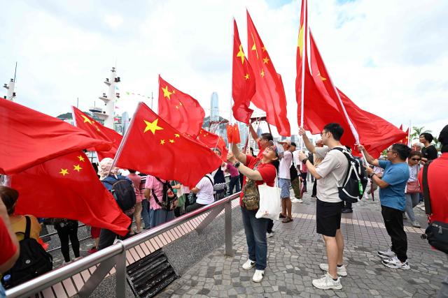 Pro-Beijing supporters wave China flags on the edge of Hong Kong's Victoria Harbour to mark the 28th anniversary of Hong Kong's handover from Britain to China in Hong Kong on July 1, 2025. (Photo by Peter PARKS / AFP)