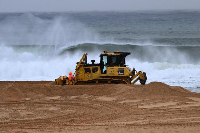 Workers operate heavy machinery to stabilise Wamberal Beach as a low-pressure cyclone lashes the Central Coast, forcing residents to evacuate beachfront homes amid growing erosion fears on July 2, 2025. (Photo by SAEED KHAN / AFP)