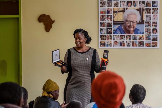 Prossy Nkayanga (C), Executive Director of Hospice Africa Uganda (HAU), shows patients the Hero's Medal awarded to Dr. Anne Merriman by the President of Uganda, in front of a poster featuring photos of Dr. Merriman at the hospice in Kampala, on June 24, 2025. Hospice Africa Uganda (HAU), founded in 1993 by Dr Anne Merriman, brought holistic end-of-life care to Uganda at a time when it was offered in only three African countries.
By the time Merriman died in May 2025, aged 90, she had treated more than 40,000 patients in Uganda and her model had spread to 37 African countries. (Photo by Badru Katumba / AFP)