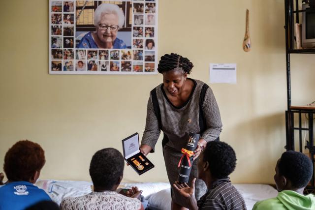 Prossy Nkayanga (C), Executive Director of Hospice Africa Uganda (HAU), shows patients the Hero's Medal awarded to Dr. Anne Merriman by the President of Uganda, in front of a poster featuring photos of Dr. Merriman at the hospice in Kampala, on June 24, 2025. Hospice Africa Uganda (HAU), founded in 1993 by Dr Anne Merriman, brought holistic end-of-life care to Uganda at a time when it was offered in only three African countries.
By the time Merriman died in May 2025, aged 90, she had treated more than 40,000 patients in Uganda and her model had spread to 37 African countries. (Photo by Badru Katumba / AFP)