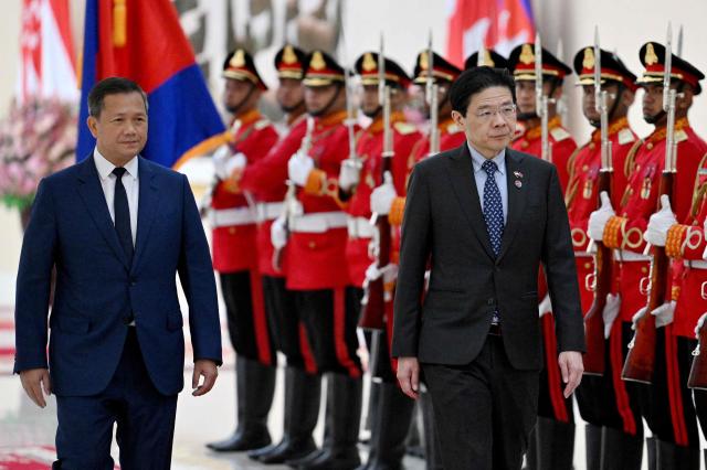 Cambodia's Prime Minister Hun Manet (L) and Singapore’s Prime Minister Lawrence Wong walk past the honour guard at the Peace Palace in Phnom Penh on July 2, 2025. (Photo by TANG CHHIN Sothy / AFP)