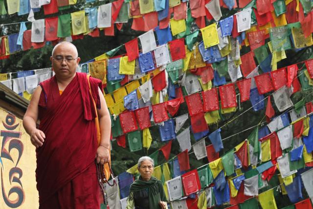 Tibetan monks walk past Buddhist prayer flags, displayed over a street in McLeod Ganj, near Dharamsala on July 2, 2025. Exiled Tibetan spiritual leader the Dalai Lama said on July 2, that the 600-year-old institution will continue after his death, a decision that will have profound impact on his Buddhist followers. (Photo by Sanjay BAID / AFP)