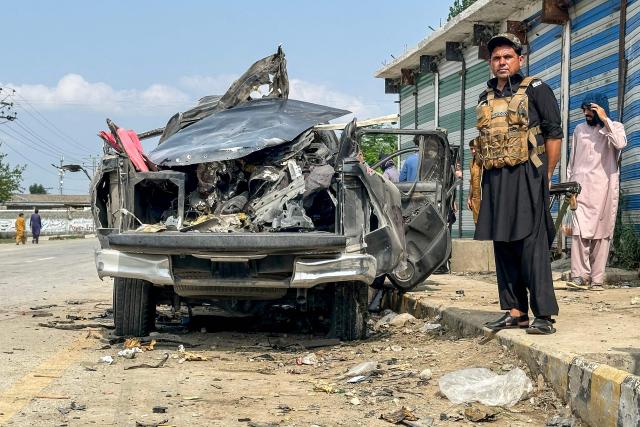 A security personnel stands guard beside the wreckage of a vehicle after a blast in Bajaur, Khyber Pakhtunkhwa province, on July 2, 2025. An explosion in northwest Pakistan on July 2 killed at least four local government and police officials, a police official told AFP. (Photo by Fazal RAHMAN / AFP)