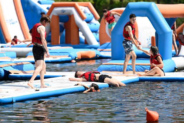 People stand on an inflatable structure at a water sports leisure centre in Basse-Ham, north-eastern France, on July 2, 2025, as a heatwave hits Europe. (Photo by Jean-Christophe VERHAEGEN / AFP)