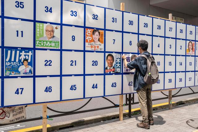 A man puts a campaign poster on a bulletin board ahead of the July 20 upper house election in Tokyo on July 3, 2025. (Photo by Yuichi YAMAZAKI / AFP)