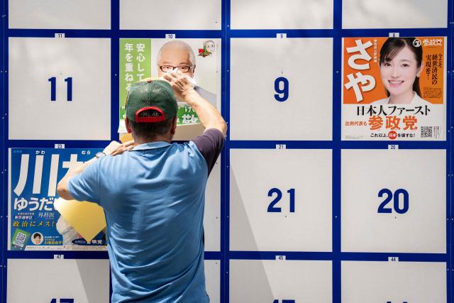 A man puts a campaign poster on a bulletin board ahead of the July 20 upper house election in Tokyo on July 3, 2025. (Photo by Yuichi YAMAZAKI / AFP)