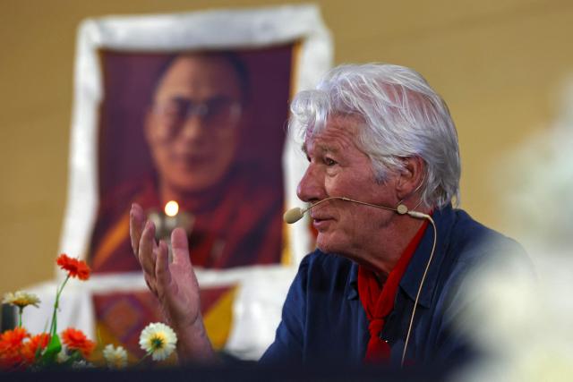 US actor Richard Gere addresses a gathering in front of a portrait of the Tibetan spiritual leader the Dalai Lama during the International Tibet Youth Forum in Dharamsala on July 3, 2025. The Dalai Lama said on July 2 that the 600-year-old Tibetan spiritual institution would continue after his death, reassuring Buddhist followers around the globe and saying his office "exclusively" would name his successor, even as China insisted it would. (Photo by Niharika KULKARNI / AFP)
