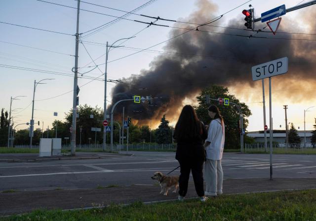 TOPSHOT - Women walk dog as smoke rises over Kyiv following mass Russian drones and missile strikes on the Ukraine's capital on July 4, 2025, amid the Russian invasion of Ukraine. Ukraine said Russia had launched 550 drones and missiles at the war-battered country overnight, as the Kremlin steps up aerial attacks and US-led peace talks stall. The Ukrainian air force said Moscow had launched 539 drones and 11 missiles, adding that air defence units had downed 268 drones and two missiles. (Photo by OLEKSII FILIPPOV / AFP)