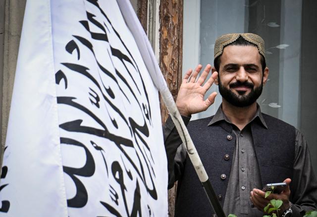 An official gestures next to the flag of the Islamic Emirate of Afghanistan as he stands on the balcony of the Afghan embassy in Moscow on July 4, 2025. Russia became the first country to recognise the Taliban's rule in Afghanistan. The Taliban swept back to power in 2021 after ousting the foreign-backed government and have imposed an austere version of Islamic law. (Photo by Alexander NEMENOV / AFP)