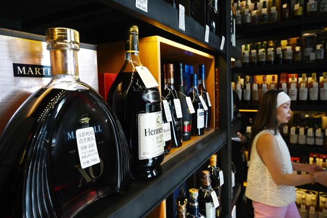 A vendor stands near cognac bottles at a liquor store in Beijing on July 4, 2025. China will require major European brandy exporters to raise prices or risk anti-dumping taxes of up to 34.9 percent from July 5, the latest salvo in its long-running trade spat with the bloc. Almost all EU brandy is cognac produced in France, exports of which to China are worth 1.4 billion euros ($1.6 billion) per year. (Photo by GREG BAKER / AFP)