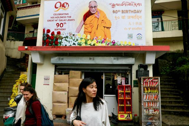 Women walk past a banner portraying the Tibetan spiritual leader Dalai Lama ahead of his 90th birthday celebrations, in McLeodganj on July 4, 2025. (Photo by Niharika Kulkarni / AFP)