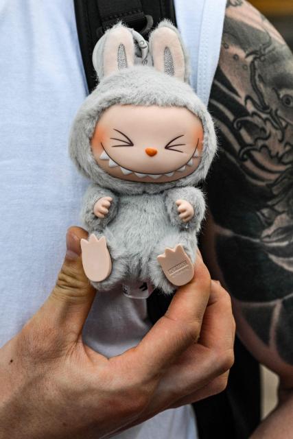 A man shows his Labubu plush toy of Pop Mart along a pedestrian street on The Bund in Shanghai on July 4, 2025. (Photo by Hector RETAMAL / AFP)