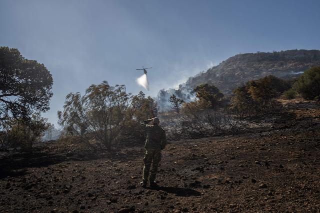 This photograph shows a helicopter dropping water on a wildfire that broke up in Koropi, some 40 Kms of Athens on July 4, 2025. The new wildfire broke out at Koropi, a town some 30 kilometres (20 miles) east of Athens, where residents received text messages from civil protection units urging them to evacuate the vicinity, on July 4, 2025. (Photo by Angelos TZORTZINIS / AFP)