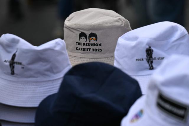 Bucket hats are seen for sale as fans of British rock band Oasis arrive at the Principality Stadium in Cardiff on July 4, 2025, to attend the opening concert of their highly anticipated reunion tour nearly 16 years after last performing together. Two consecutive nights of concerts at the Principality Stadium in the Welsh capital mark the start of a 41-date run of gigs spanning the world. (Photo by Oli SCARFF / AFP)