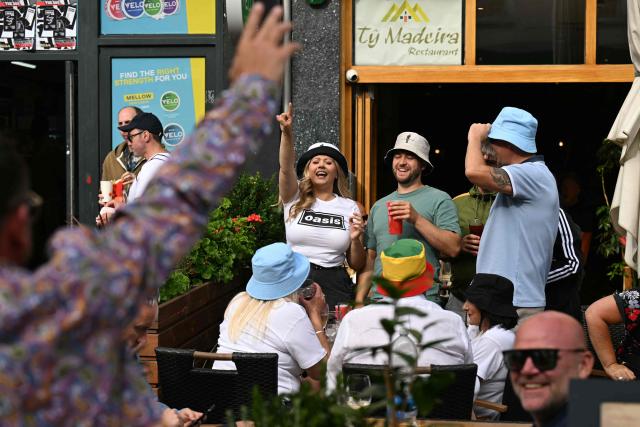 Fans of British rock band Oasis enjoy a drink outside a pub in Cardiff on July 4, 2025, ahead of the opening concert of their highly anticipated reunion tour nearly 16 years after last performing together. Two consecutive nights of concerts at the Principality Stadium in the Welsh capital mark the start of a 41-date run of gigs spanning the world. (Photo by Oli SCARFF / AFP)
