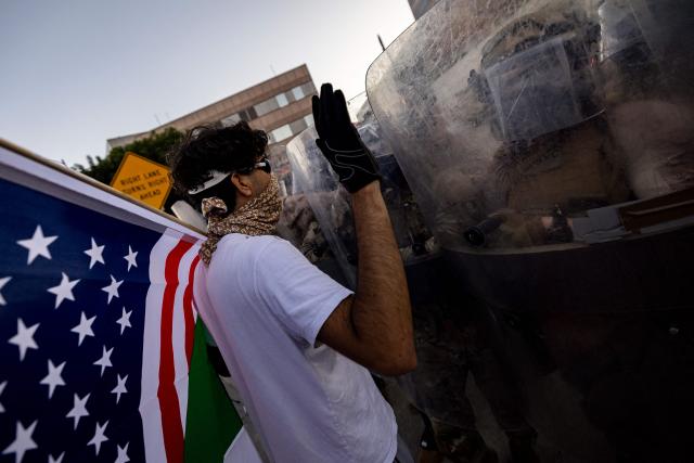 A demonstrator interacts with US marines and national guards standing in line protecting the entrance of the Metropolitan Detention Center as demonstrators gather in front of it following federal immigration operations, in Los Angeles, California on July 4, 2025. (Photo by Etienne LAURENT / AFP)
