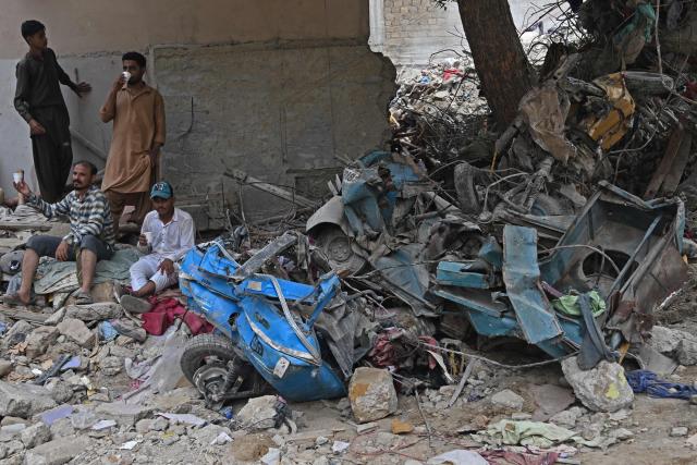 Local residents sir amid the debris of a collapsed residential building in Karachi on July 5, 2025. Rescue teams pulled more bodies from the rubble of a five-storey building collapse in Pakistan overnight, taking the toll on July 5 to 14 as the recovery operation continued for a second day. (Photo by Rizwan TABASSUM / AFP)