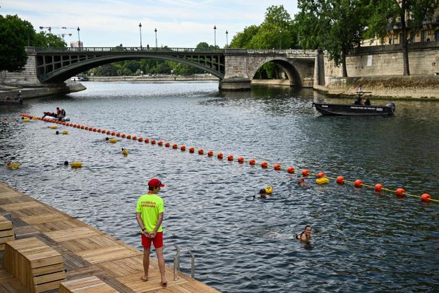 A lifeguard stands on duty as people swim at the Pont Marie safe bathing site on the Seine river on its opening day, in Paris on July 5, 2025. The River Seine reopened to Parisian swimmers this morning for the first time since 1923, offering locals and tourists a welcome respite after scorching temperatures. The seasonal opening of the Seine for swimming is seen as a key legacy of the Paris 2024 Olympics, when open water swimmers and triathletes competed in its waters which were specially cleaned for the event. (Photo by JULIEN DE ROSA / AFP)