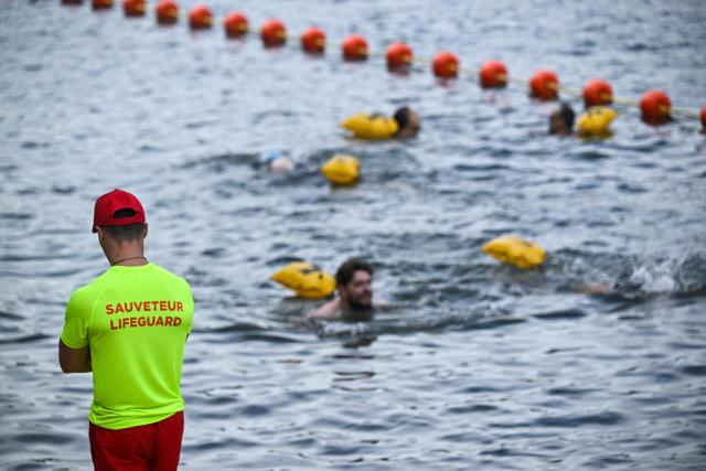 A lifeguard stands on duty as people swim at the Pont Marie safe bathing site on the Seine river on its opening day, in Paris on July 5, 2025. The River Seine reopened to Parisian swimmers this morning for the first time since 1923, offering locals and tourists a welcome respite after scorching temperatures. The seasonal opening of the Seine for swimming is seen as a key legacy of the Paris 2024 Olympics, when open water swimmers and triathletes competed in its waters which were specially cleaned for the event. (Photo by JULIEN DE ROSA / AFP)