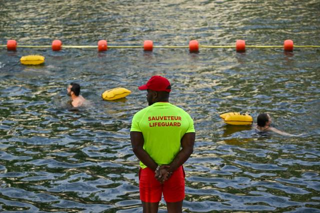 A lifeguard stands on duty as people swim at the Pont Marie safe bathing site on the Seine river on its opening day, in Paris on July 5, 2025. The River Seine reopened to Parisian swimmers this morning for the first time since 1923, offering locals and tourists a welcome respite after scorching temperatures. The seasonal opening of the Seine for swimming is seen as a key legacy of the Paris 2024 Olympics, when open water swimmers and triathletes competed in its waters which were specially cleaned for the event. (Photo by JULIEN DE ROSA / AFP)