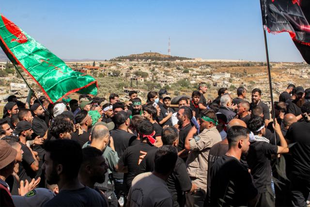 The Israeli town of Metulla across the border is pictured in the background as Shiite Muslim worshippers walk in a mourning procession in Lebanon's southern village of Kfarkila on July 5, 2025, which coincides with the ninth day of the Islamic month of Muharram in the lead-up to Ashura, a 10-day period commemorating the seventh century killing of Prophet Mohammed's grandson Imam Hussein. (Photo by Rabih DAHER / AFP)