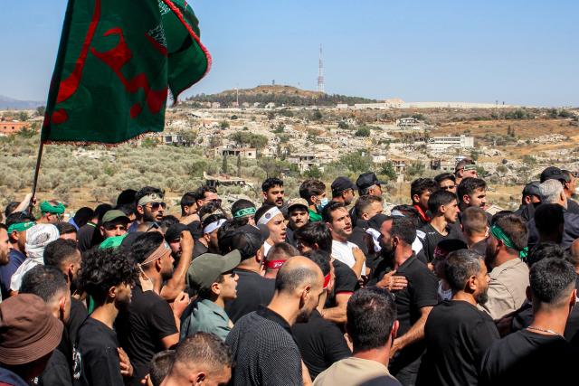 The Israeli town of Metulla across the border is pictured in the background as Shiite Muslim worshippers walk in a mourning procession in Lebanon's southern village of Kfarkila on July 5, 2025, which coincides with the ninth day of the Islamic month of Muharram in the lead-up to Ashura, a 10-day period commemorating the seventh century killing of Prophet Mohammed's grandson Imam Hussein. (Photo by Rabih DAHER / AFP)