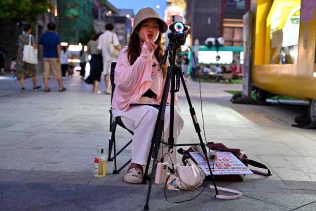 A woman live streams from a phone, in the Qianmen promenade in Beijing on July 5, 2025. (Photo by Adek BERRY / AFP)