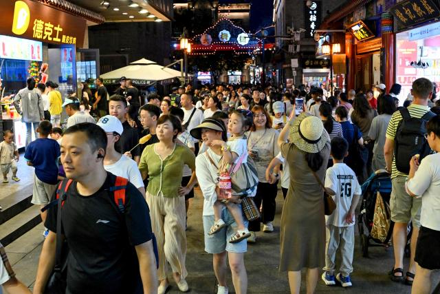 People walk along Qianmen promenade in Beijing on July 5, 2025. (Photo by Adek BERRY / AFP)