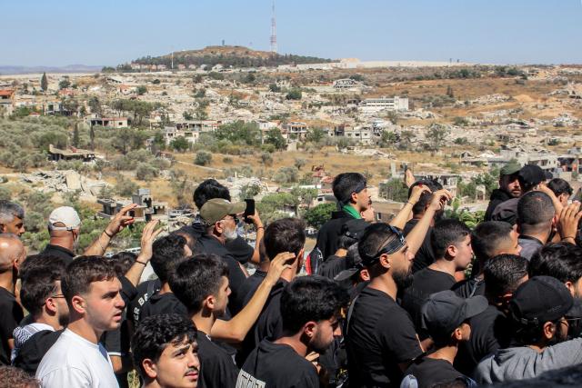 The Israeli town of Metulla across the border is pictured in the background as Shiite Muslim worshippers walk in a mourning procession in Lebanon's southern village of Kfarkila on July 5, 2025, which coincides with the ninth day of the Islamic month of Muharram in the lead-up to Ashura, a 10-day period commemorating the seventh century killing of Prophet Mohammed's grandson Imam Hussein. (Photo by Rabih DAHER / AFP)