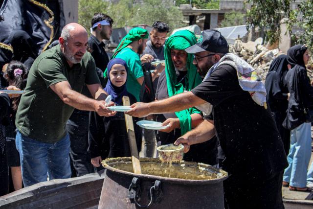 Shiite Muslim worshippers are handed over charity meals during a mourning procession in Lebanon's southern village of Kfarkila near the border with Israel on July 5, 2025, which coincides with the ninth day of the Islamic month of Muharram in the lead-up to Ashura, a 10-day period commemorating the seventh century killing of Prophet Mohammed's grandson Imam Hussein. (Photo by Rabih DAHER / AFP)