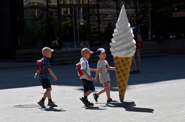 Boys walk past a large advertising ice cream model during hot summer day in Ukrainian capital of Kyiv on July 5, 2025, amid Russian invasion in Ukraine. (Photo by Sergei SUPINSKY / AFP)