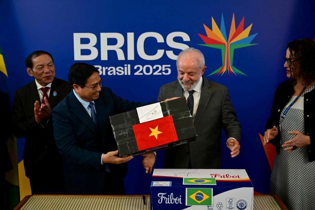 Vietnam's Prime Minister Pham Minh Chinh (L) gives a signed box of Navico (also known as Nam Viet Corporation, a major Vietnamese seafood producer and exporter) to Brazil's President Luiz Inacio Lula da Silva as they celebrate the completion of the first export of Brazilian beef to Vietnam and the first export of Vietnamese tilapia to Brazil after a bilateral meeting ahead of the BRICS summit in Rio de Janeiro, Brazil, on July 5, 2025. BRICS leaders meeting in Rio de Janeiro from Sunday are expected to decry Donald Trump's hardline trade policies, but are struggling to bridge divides over crises roiling the Middle East. (Photo by Pablo PORCIUNCULA / AFP)