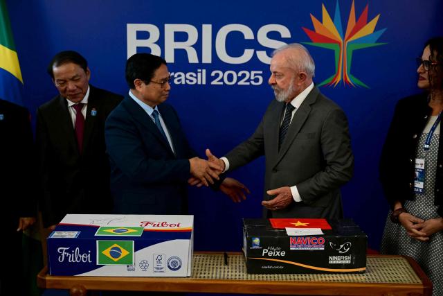 Vietnam's Prime Minister Pham Minh Chinh (L) shakes hands with Brazil's President Luiz Inacio Lula da Silva as they celebrate the completion of the first export of Brazilian beef to Vietnam and the first export of Vietnamese tilapia to Brazil after a bilateral meeting ahead of the BRICS summit in Rio de Janeiro, Brazil, on July 5, 2025. BRICS leaders meeting in Rio de Janeiro from Sunday are expected to decry Donald Trump's hardline trade policies, but are struggling to bridge divides over crises roiling the Middle East. (Photo by Pablo PORCIUNCULA / AFP)