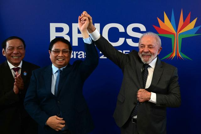 Vietnam's Prime Minister Pham Minh Chinh (L) and Brazil's President Luiz Inacio Lula da Silva hold hands as they celebrate the completion of the first export of Brazilian beef to Vietnam and the first export of Vietnamese tilapia to Brazil after a bilateral meeting ahead of the BRICS summit in Rio de Janeiro, Brazil, on July 5, 2025. BRICS leaders meeting in Rio de Janeiro from Sunday are expected to decry Donald Trump's hardline trade policies, but are struggling to bridge divides over crises roiling the Middle East. (Photo by Pablo PORCIUNCULA / AFP)