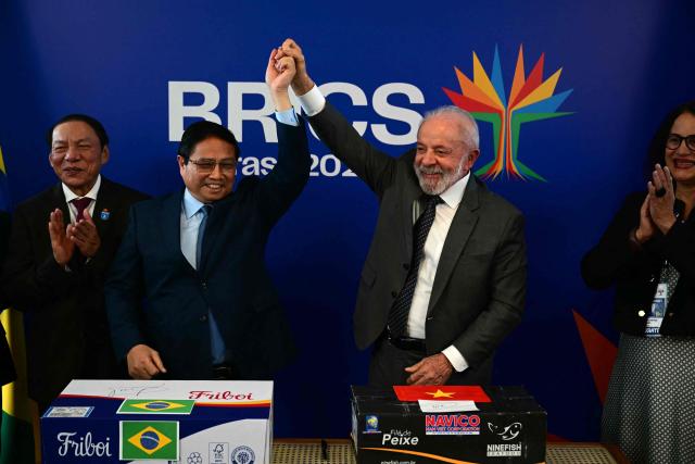 Vietnam's Prime Minister Pham Minh Chinh (L) and Brazil's President Luiz Inacio Lula da Silva hold hands as they celebrate the completion of the first export of Brazilian beef to Vietnam and the first export of Vietnamese tilapia to Brazil after a bilateral meeting ahead of the BRICS summit in Rio de Janeiro, Brazil, on July 5, 2025. BRICS leaders meeting in Rio de Janeiro from Sunday are expected to decry Donald Trump's hardline trade policies, but are struggling to bridge divides over crises roiling the Middle East. (Photo by Pablo PORCIUNCULA / AFP)