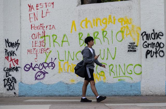 A man walks past a wall with graffiti a day after a march against gentrification and the increasing presence of US citizens in the La Condesa neighbourhood of Mexico City at Mexico Park on July 5, 2025. Shouting "gringos out!" and waving banners and vandalizing various businesses, hundreds of people demonstrated this Friday in Mexico City against the gentrification of various neighborhoods due to the arrival of foreigners. (Photo by Yuri CORTEZ / AFP)