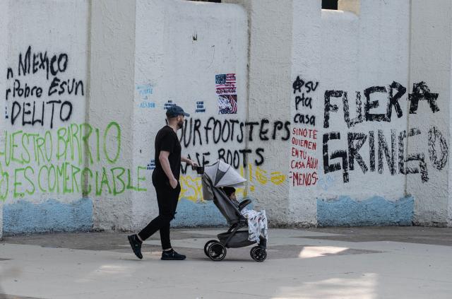 A man walks in front of a wall of Mexico Park with graffiti a day after a march against gentrification and the increasing presence of US citizens in the La Condesa neighbourhood of Mexico City on July 5, 2025. Shouting "gringos out!" and waving banners and vandalizing various businesses, hundreds of people demonstrated this Friday in Mexico City against the gentrification of various neighborhoods due to the arrival of foreigners. (Photo by Yuri CORTEZ / AFP)